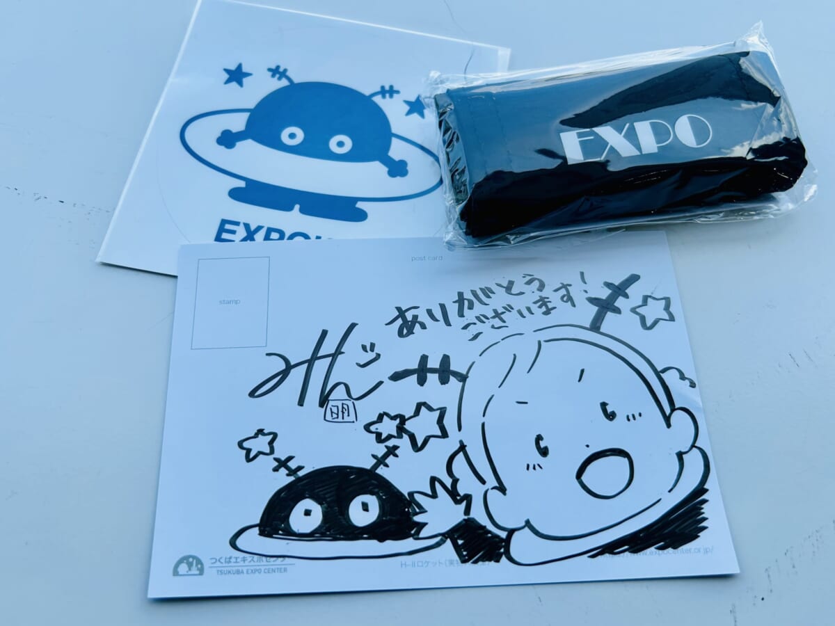 「コスモ星丸」のステッカー&エコバックと、明さんの「イラスト&サイン入りポストカード」をセットに。