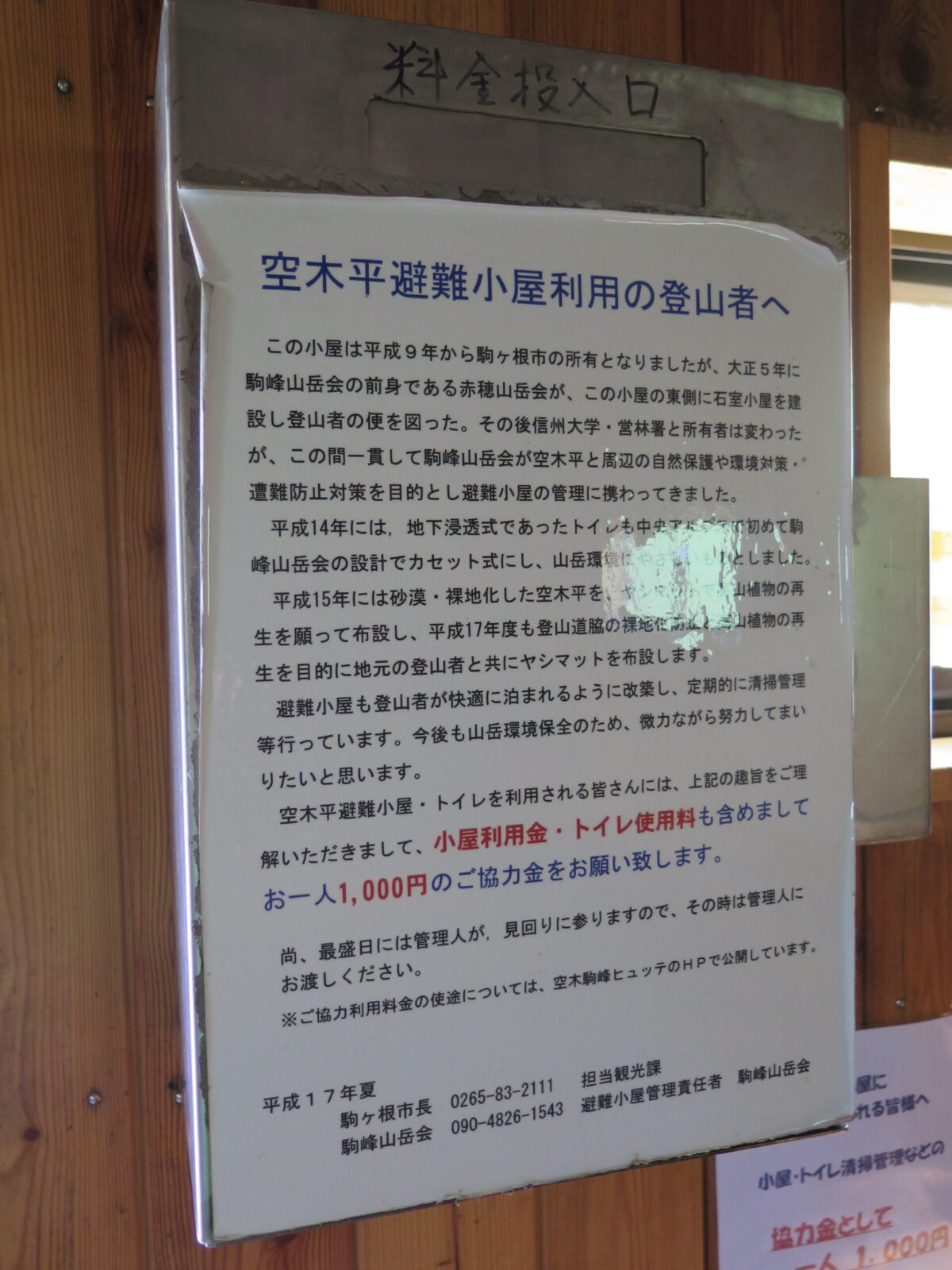 小屋内に掲示された小屋の歴史の説明と登山者へのメッセージ。その上に料金投入口もある