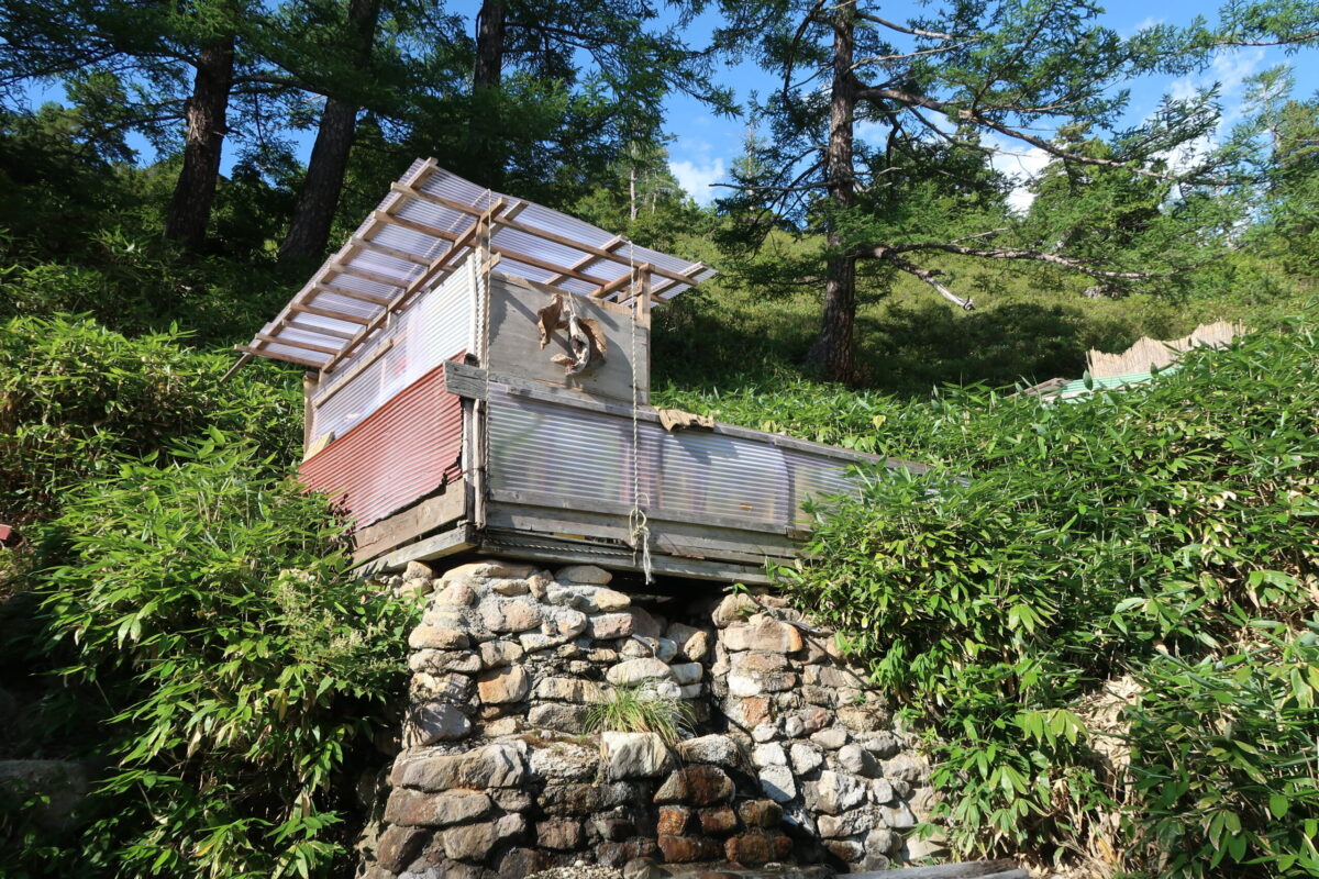 右岸の混浴露天風呂を外側から。湯船からあふれた温泉は積み上げた石の壁伝いに沢へ流れ出していた