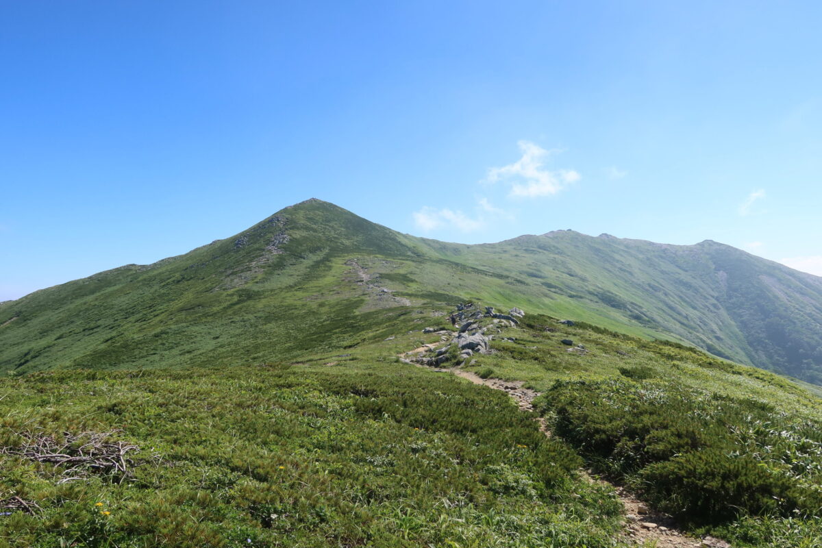 御西岳のほうから飯豊山を眺めた様子。左の小高い場所が飯豊本山で、そこから緩く起伏しながら右に延びる稜線がだんだん低くなり始めるあたりに、飯豊山神社奥宮と本山小屋がある