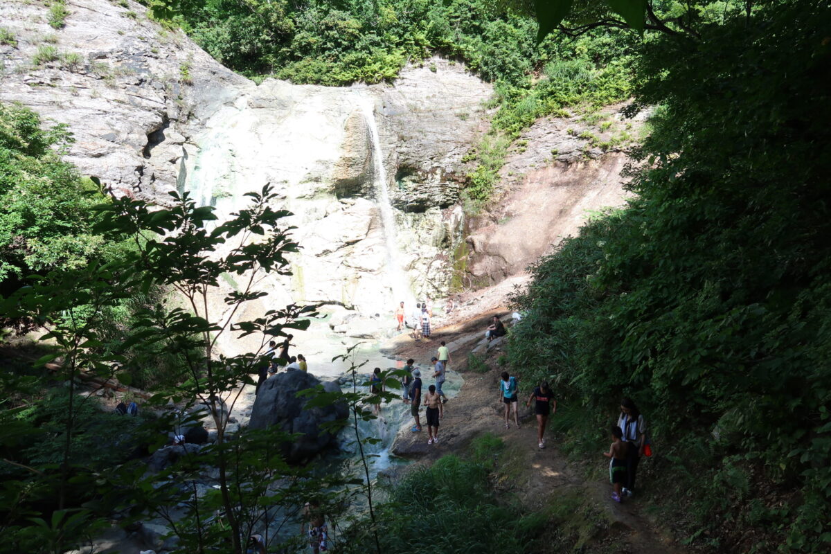 登山道を慎重に下りていくと、遠くに川原毛大湯滝が流れ落ちる巨大な岩盤が見えてくる